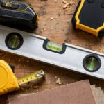 Drill, stud finder, level, tape measure and sandpaper laid out as DIY shelf tools