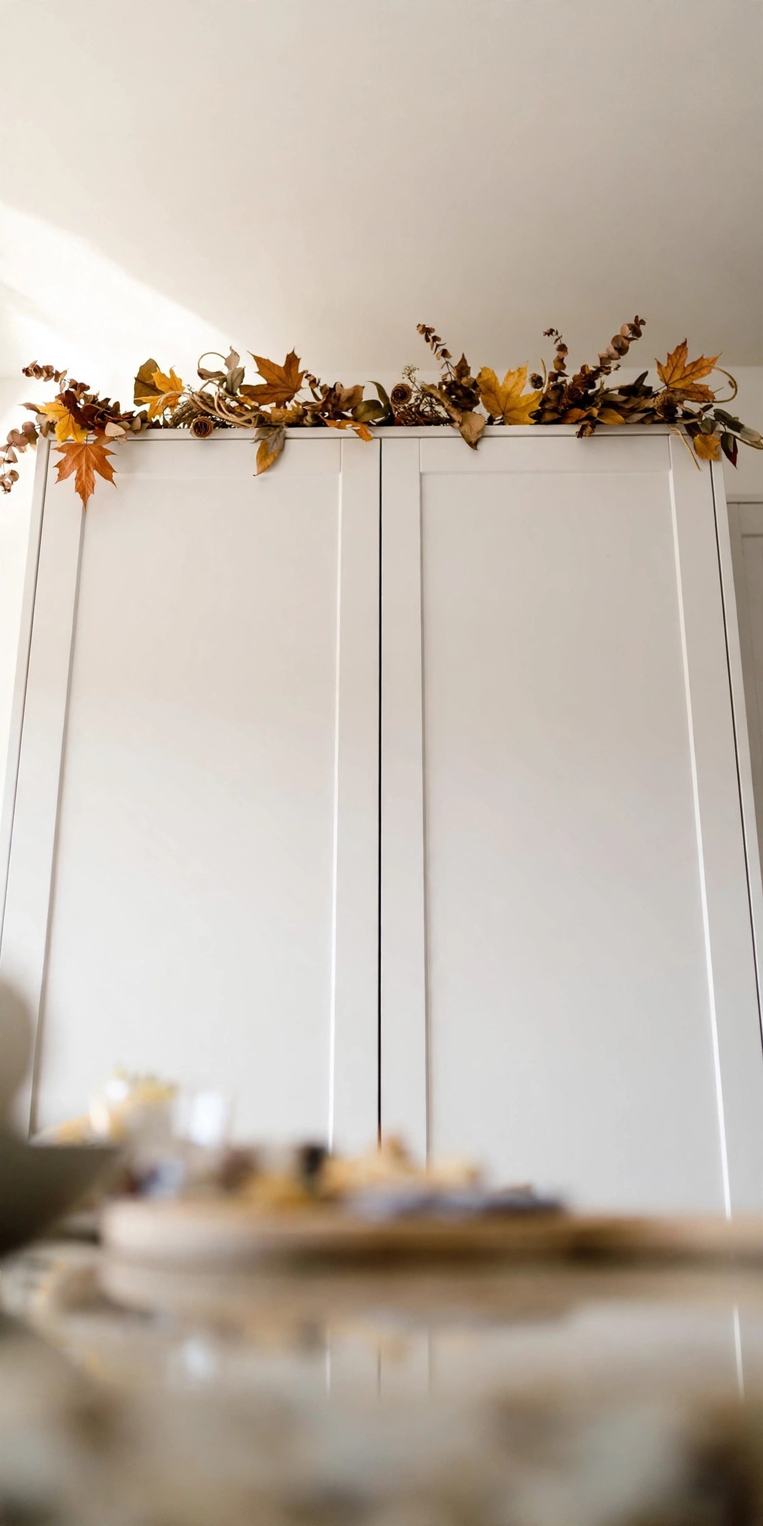 Dried-leaf garland resting along the tops of white kitchen cabinets